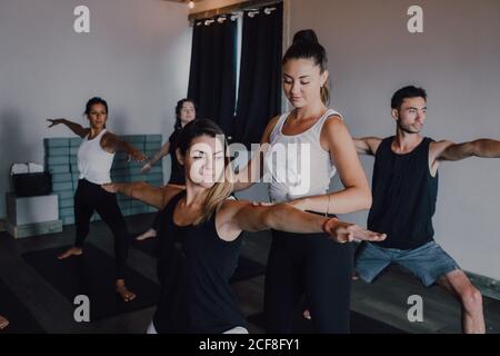 Lächelnd fleißig weibliche Ausbilderin Sportswear Unterricht Krieger Pose zwei Gruppe von sportlichen Menschen tun Übung stehen auf Sportmatten Im modernen Fitnessraum Stockfoto