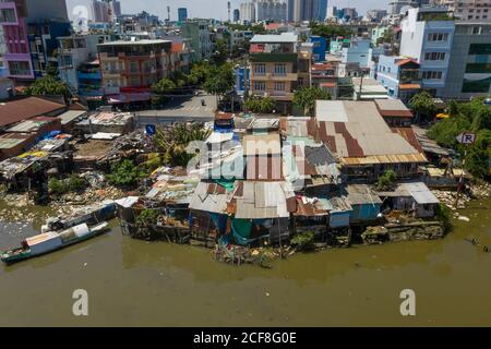 Alte Hütten aus Wellblech im Gegensatz zu modernen Gebäuden am Ufer des Kenh Te Canal in Ho Chi Minh City, Vietnam Stockfoto