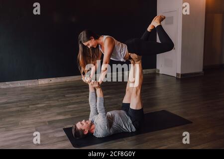 High-Angle-Seitenansicht von glücklichen jungen barfüßigen Paar in activewear, die einander anblicken und lächeln, während sie Balance halten Trainieren Sie im modernen Stil in der Plankenposition auf dem Boden studio Stockfoto
