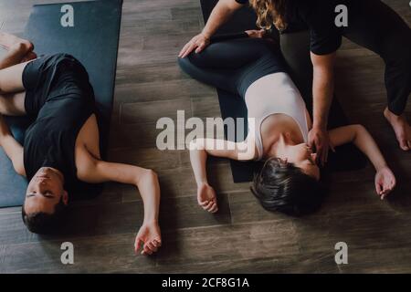 Hoher Winkel der Gruppe der jungen sportlichen Frauen und Männer In der Sportbekleidung mit geschlossenen Augen und gekreuzten Beinen entspannend und Tiefes Atmen, während man in Savasana-Position liegt und meditiert Sportmatten im modernen Yoga-Studio Stockfoto