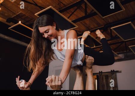 High-Angle-Seitenansicht von glücklichen jungen barfüßigen Paar in activewear, die einander anblicken und lächeln, während sie Balance halten Trainieren Sie im modernen Stil in der Plankenposition auf dem Boden studio Stockfoto