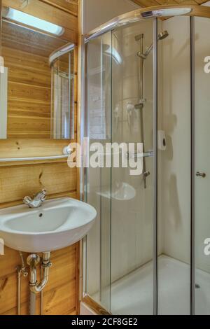 Innenraum des Badezimmers mit Holzwänden mit Keramikwaschbecken ausgestattet Und Duschkabine aus Glas Stockfoto