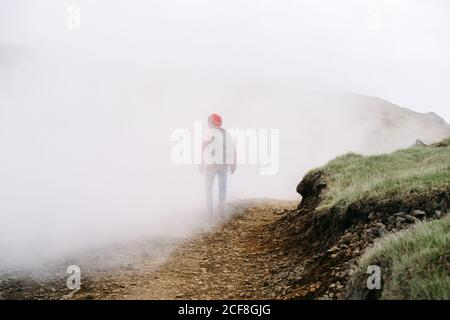 Rückansicht eines anonymen männlichen Entdeckers, der die Straße entlang geht Berge bei nebligen Wetter in Island Stockfoto