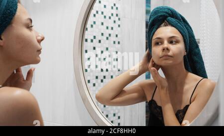 Junge Frau hat Probleme mit der Haut im Gesicht - Sie schaut in den Spiegel im Badezimmer Stockfoto