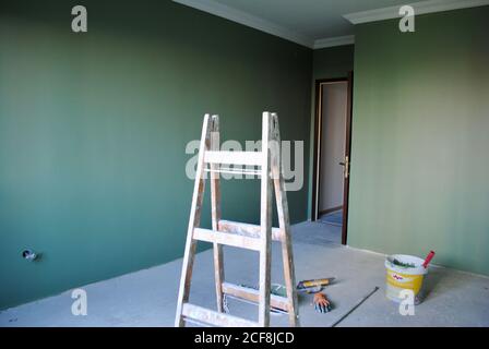 Das Zimmer wurde renoviert und die Wände sind dunkelgrün gestrichen. Leiter, Farbeimer, Handschuhe und Spachtel auf dem Boden. Sanierungskonzept mit Kopierfläche. Stockfoto