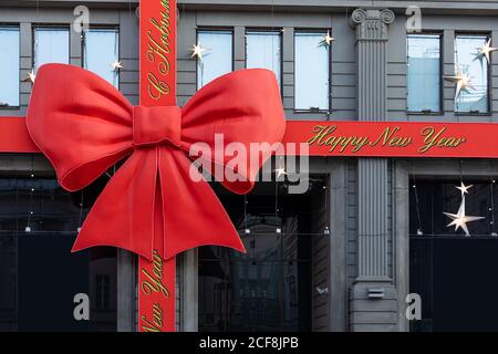 Weihnachtsdekoration auf dem Gebäude. Rotes Band mit Inschrift Frohe Weihnachten und ein glückliches neues Jahr und eine große Schleife. Gebäude als Geschenk gebunden roten Satin Stockfoto