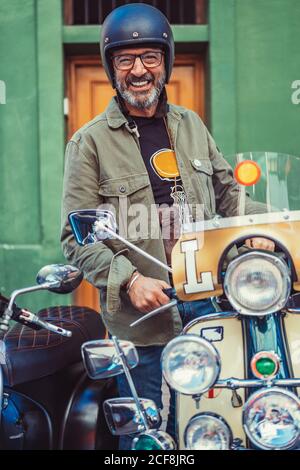Bärtiger reifer Mann in Helm und Brille sitzt auf Custom Motorrad mit vielen Scheinwerfern auf der Stadtstraße Stockfoto