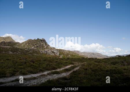 Traillinien am Boden durchqueren ein grünes Hochland mitten in den Bergen, mit Wolken am Horizont Stockfoto