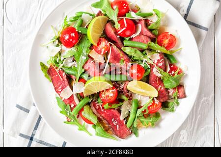 Steak-Salat aus saftigen seltenen Rindsfilet Steak in der Pfanne gebraten und in Scheiben geschnitten, Rucola, Kirschtomaten, grüne Bohnen, Parmesan-Käse auf einem weißen Teller mit l serviert Stockfoto