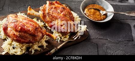 Gebratenes oder gegrilltes Eisbein, oder Schinkenhacke oder Knöchel, auf Sauerkraut auf rustikalen Ziegeln mit Sauce als Beilage Stockfoto