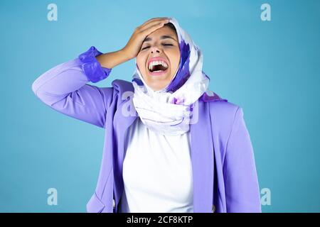 Junge schöne arabische Frau trägt islamischen Hijab über isoliert blau Hintergrund lachend mit der Hand auf dem Kopf, wie sie vergessen Etwas Stockfoto