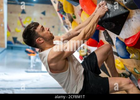 Seitenansicht des starken männlichen Athleten in der Sportbekleidung beim Klettern Bunte Wand während des Trainings in modernen Kerl Stockfoto