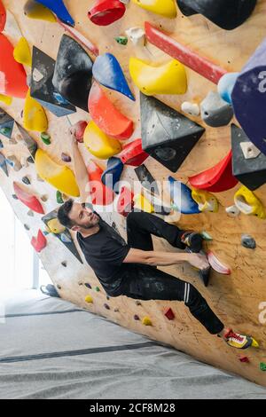 Von bellow starken männlichen Athleten in Sportbekleidung Klettern auf bunt Wand während des Trainings in modernen Kerl Stockfoto