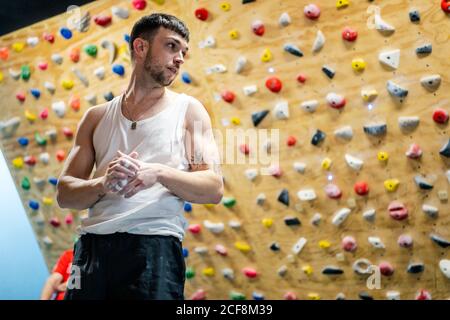 Von unten von jungen Mann in Sportbekleidung stehen und suchen Weg mit Kletterwand auf verschwommenem Hintergrund Stockfoto