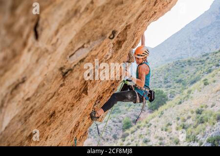 Von unten Ansicht der aktiven fokussierten Jugendlichen Alpinistin Klettern auf Klippen im Sommer Tag Stockfoto