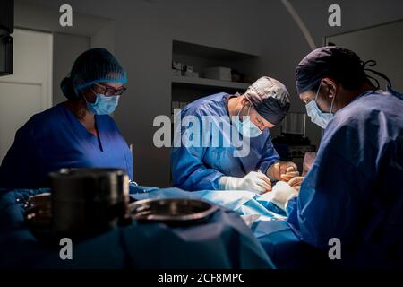 Chirurgen und Krankenschwestern in einheitlicher Konzentration und Operation Patienten mit Spezielle Ausrüstung im Operationssaal des zeitgenössischen Krankenhauses Stockfoto