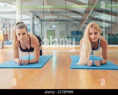 Zwei muskulöse schlanke Frauen in Sportkleidung, die während der Kamera Machen Plank auf Matte im Fitness-Studio Stockfoto