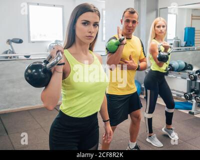 Starke Männer und Frauen beim Heben von Kettlebells während des Trainings im Fitnessstudio Stockfoto