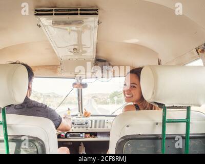 Rückansicht eines unkenntlichen Fahrers und einer jungen lächelnden Frau, die im Auto vor der Kamera sitzt Stockfoto