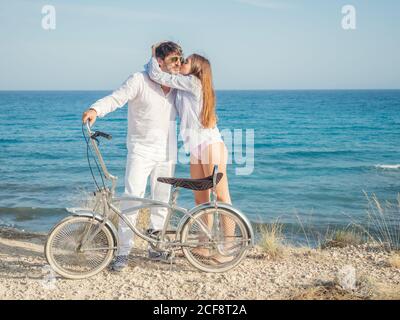 Stilvoller Mann und junge Frau, die an der Küste mit dem Fahrrad stehen und die herrliche Meereslandschaft an einem hellen Tag genießen Stockfoto