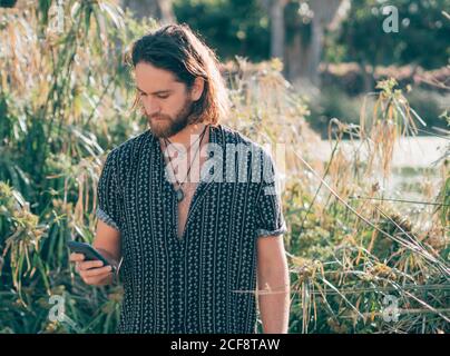 Junge bärtige Hipster Mann trägt T-Shirt SMS auf Handy Im tropischen Dschungel Stockfoto