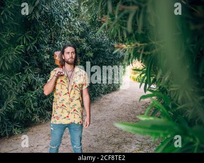 Nachdenklicher bärtiger Hipster-Mann, der mit Ukulele im Dschungel läuft Stockfoto