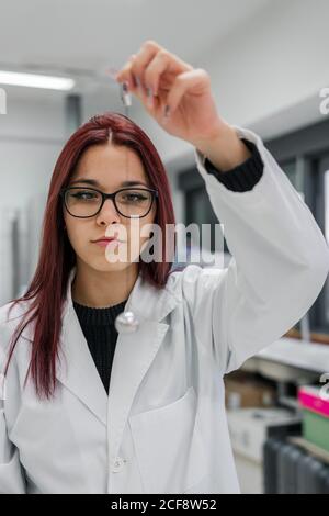 Junge Frau mit rotem Haar führt ein Experiment mit Pendel durch, während sie im zeitgenössischen Labor arbeitet Stockfoto