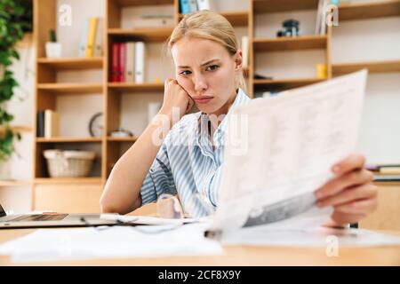 Bild von müde blonde Frau arbeiten mit Papieren und Laptop Am Tisch im Büro Stockfoto