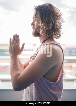 Bärtiger Mann in Sportkleidung, der in einem Bein mit Gebet steht Hände, die auf dem blauen Boden im Studio wegschauen Stockfoto