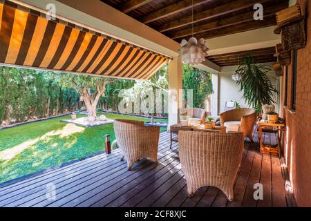 Holztisch mit Stühlen auf der großen Gartenterrasse platziert Modernes Landhaus umgeben von grünen Pflanzen Stockfoto