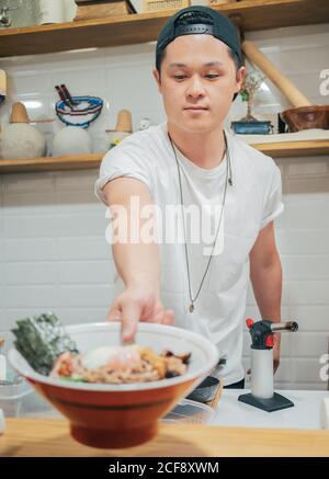 Junge männliche Koch setzen auf der Theke große Schüssel mit köstlichen Japanisches Gericht namens Ramen im orientalischen Café Stockfoto