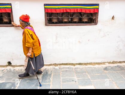 NEPAL, BOUDHANATH STUPA - 19. AUGUST 2014: Seitenansicht einer älteren Frau, die mit Gehstock in die Nähe der Wand des alten Gebäudes geht Stockfoto