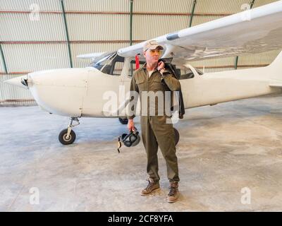 Selbstbewusster Pilot neben Retro-Flugzeug im Hangar Stockfoto