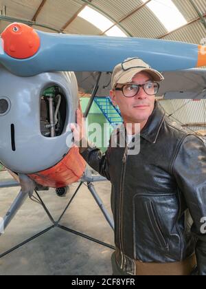 Selbstbewusster Pilot neben Retro-Flugzeug im Hangar Stockfoto