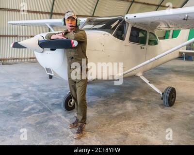 Selbstbewusster Pilot neben Retro-Flugzeug im Hangar Stockfoto
