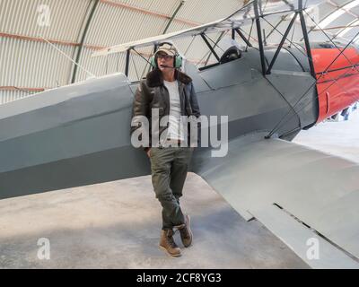 Selbstbewusster Pilot neben Retro-Flugzeug im Hangar Stockfoto