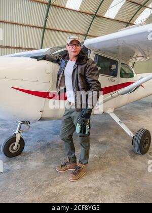 Selbstbewusster Pilot neben Retro-Flugzeug im Hangar Stockfoto