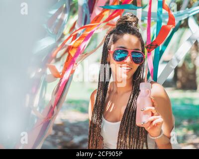 Stilvolle junge Frau trägt Sonnenbrille fürchten trinken Cocktail während draußen festival und Blick auf die Kamera Stockfoto