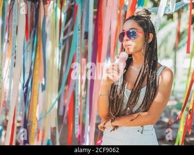 Stilvolle junge Frau trägt Sonnenbrille fürchten trinken Cocktail während draußen festival und wegschauen Stockfoto