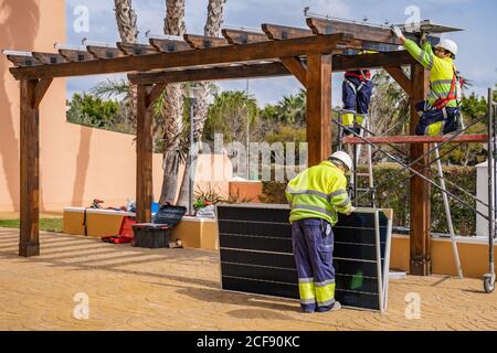 Gruppe von Arbeitern in Uniform und Helme Installation von Photovoltaik-Panels Auf dem Dach der Holzkonstruktion neben dem Haus Stockfoto