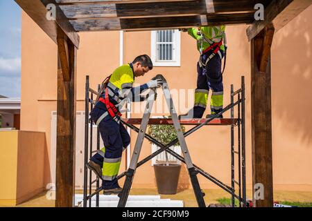 Gruppe von Arbeitern in Uniform und Helme Installation von Photovoltaik-Panels Auf dem Dach der Holzkonstruktion neben dem Haus Stockfoto