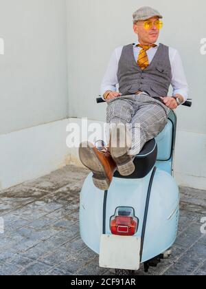 Positiver Hipster mittleren Alters in eleganter Kleidung, die auf einem Retro-Look ruht Motorrad schaut weg in sonnigen Tag Stockfoto