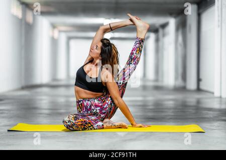 Ganzkörper junge flexible weibliche in aktiven tragen sitzen in Kompass Pose und Stretching Muskeln während Yoga in der Garage üben Halle Stockfoto