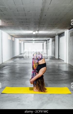 Seitenansicht von anonymous fit female in Sportswear, die nach vorne steht Bend Pose während Yoga in Licht Garage Halle üben Stockfoto