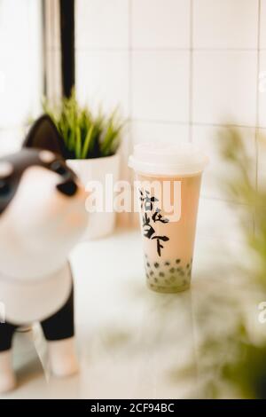 Leckere Milch Bubble Tee mit Tapioka Perlen in Kunststoff-Tasse Auf dem Tisch in der Nähe von Topfpflanzen im traditionellen taiwanesischen Café Stockfoto