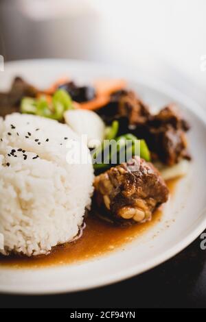 Zubereitete leckere heiße Schweinefleischrippen mit Reis und gesundem Gemüse Wie Gurken und Zwiebeln auf dem Teller im asiatischen Restaurant Stockfoto