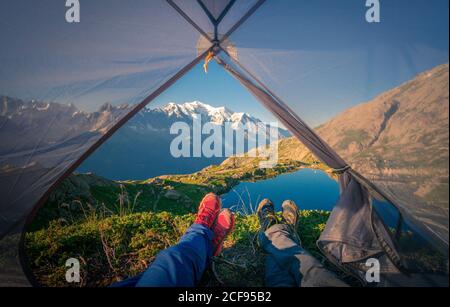 Ernte angenehme Wanderer in bunten Turnschuhen liegend mit gekreuzten Beinen in kleinen transparenten Zelt in der Nähe klaren See in den Bergen in sonnigen Tag in Chamonix, Mont-Blanc Stockfoto