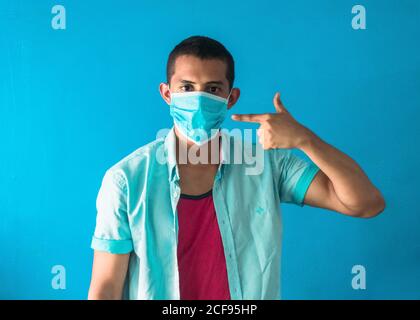 Junger Mann in einer schützenden Gesichtsmaske gestikulierenden Selbstmord isoliert Auf blauem Hintergrund Stockfoto