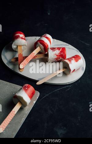 Mehrere Wassermelonen und Cremepopsicles legen auf ausgefallene Gerichte auf Dunkler Hintergrund Stockfoto