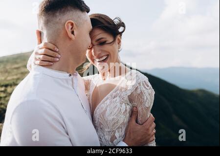 Schöne fabelhafte glückliche Braut und stilvollen Bräutigam posiert auf dem Hintergrund der sonnigen atemberaubenden Berge. Stockfoto